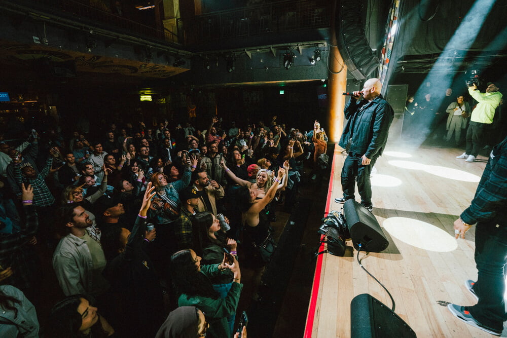 A packed audience at a concert, with Fat Joe performing on stage, engaging the enthusiastic crowd, organised by emc3, a global events agency