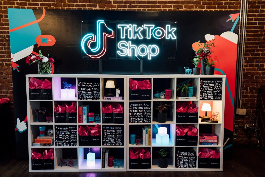 A stylish display setup featuring TikTok Shop merchandise. The illuminated TikTok Shop sign and vibrant gift bags create an appealing and modern aesthetic.