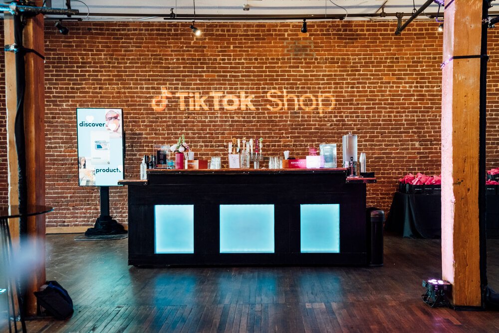 An inviting bar setup with a modern touch, featuring the TikTok Shop logo projected onto a rustic brick wall. The ambiance is perfect for a social event.