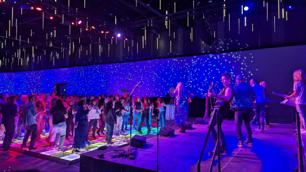 People dancing on a lit-up floor in front of a band with starry wall projections at Microsoft SOAR